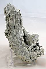 Abb.zeigt ein 20 cm langes und 5 cm breites Granitgestein ist an einem Ende um 90° gebogen, im innen Radius der Bigung sitz ein 5 cm großer Bergkristall.