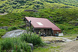 Mitten im Grünen steht die Hütte mit rotbraunem Dach.