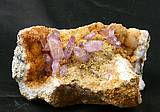 Abb. zeigt eine 10 cm breite Amethyststufe , die amethyste sind violett und sitzen auf bräunlich wirkenden kleiner Calcitkristallen.