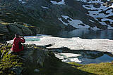 Strahler mit roter Jacke am tiefblauen mit Eis bedcktem Blausee.